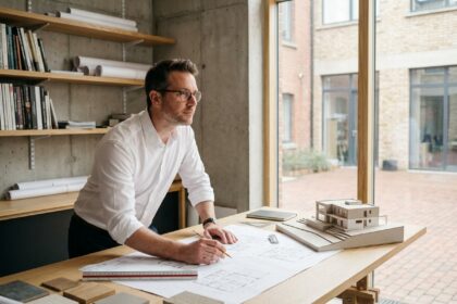 Architecte masculin étudiant des plans de construction détaillés sur une grande table de travail en bois dans un studio professionnel